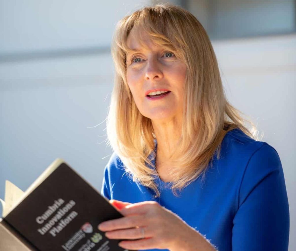 CUSP II lead Sarah Allison holds a book as she speaks. She is wearing a blue blouse and has blonde hair
