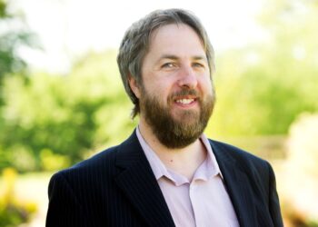 Man with a beard smiling outdoors.