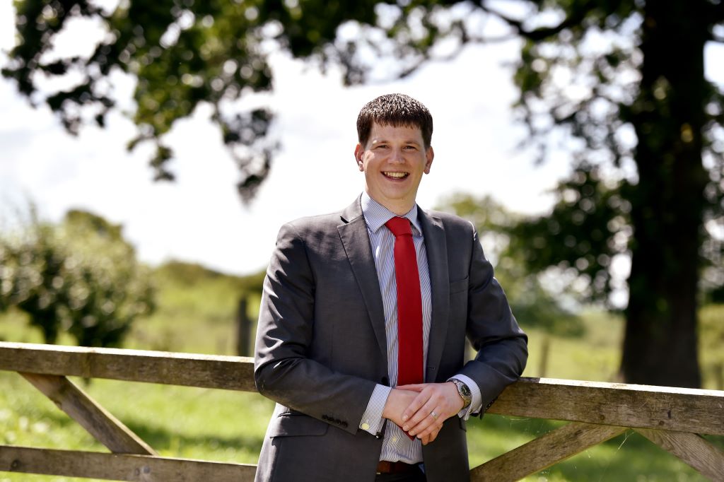 Man in suit and red tie, smiling outdoors.