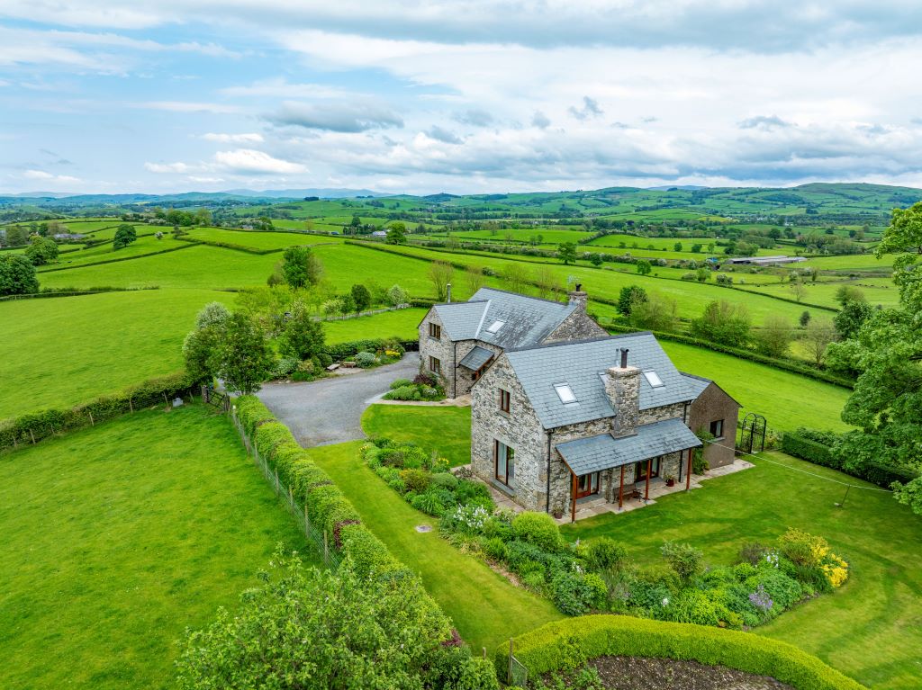Aerial view of stone cottage in lush countryside.