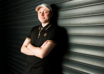 Person in black shirt and white cap, arms crossed, smiling.