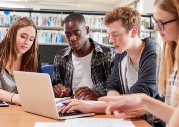 Students collaborating in a library with a laptop.