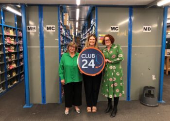 Three women posing with a Club 24 sign.