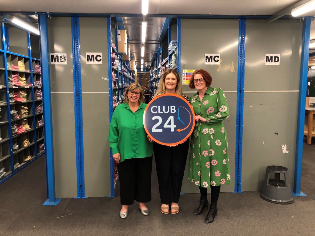 Three women posing with a Club 24 sign.