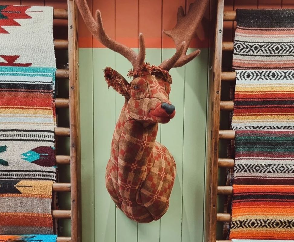 Plaid reindeer head between colourful woven blankets on wooden racks.