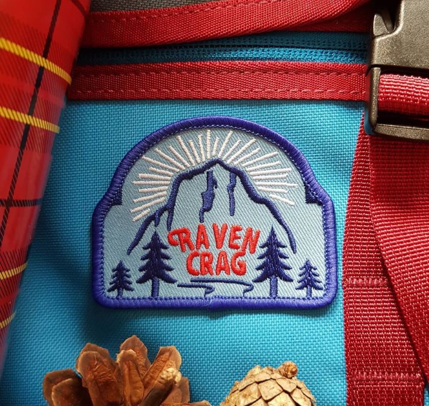 Raven Crag embroidered patch on backpack with pine cones.