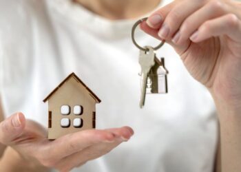 Holding house model and keys, symbolising property ownership.