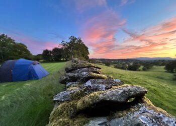 Tent on field at sunset, stone wall foreground