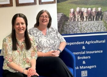 Two women sitting beside insurance company banner.
