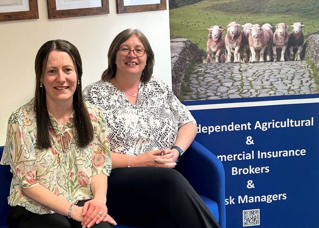Two women sitting beside insurance company banner.