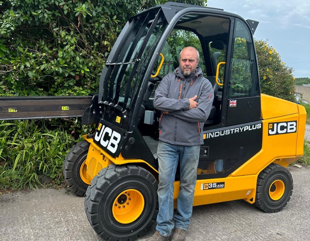 Man standing beside JCB forklift outdoors.