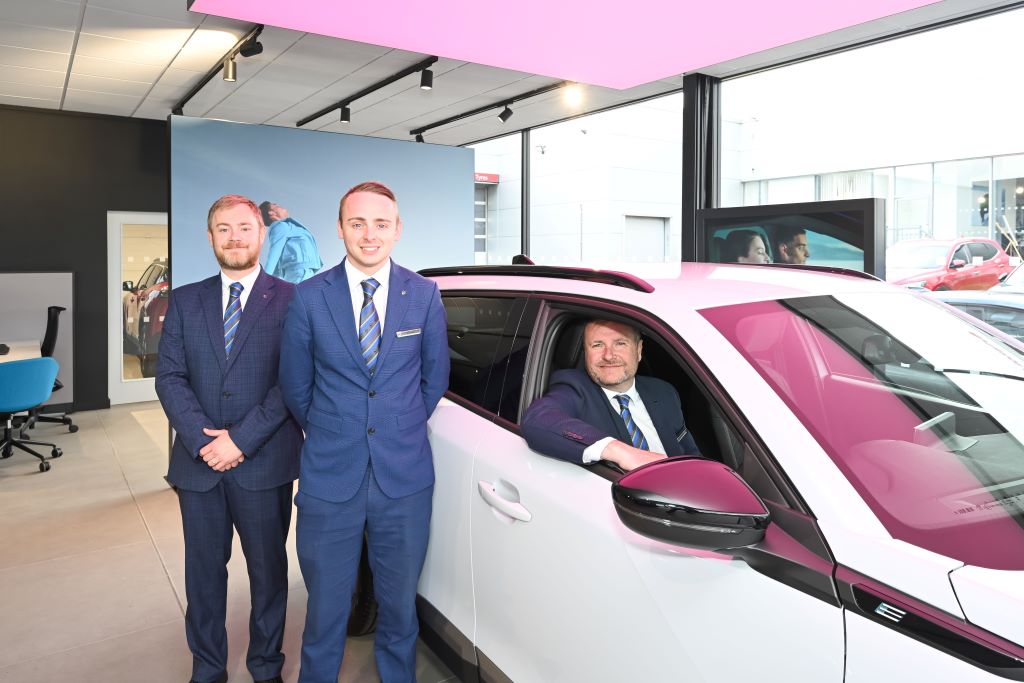 Three men in a car showroom.