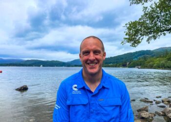 Man by Lake District lake in blue shirt.