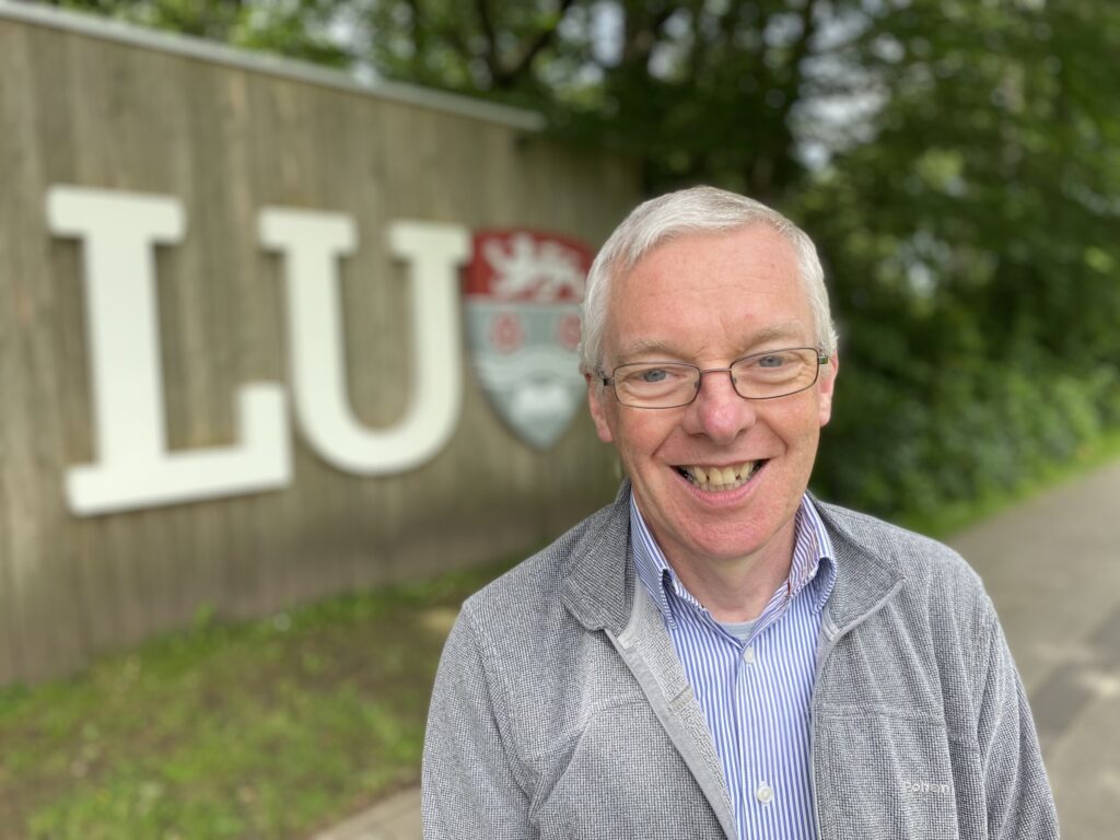 Man smiling in front of LU sign