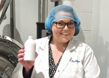 Smiling worker holding product in manufacturing facility.