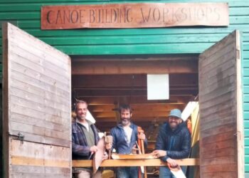 Three men at canoe building workshop.