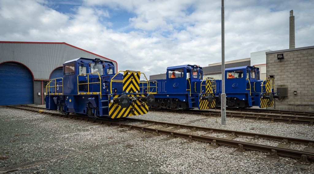 Blue diesel locomotives parked outside a warehouse