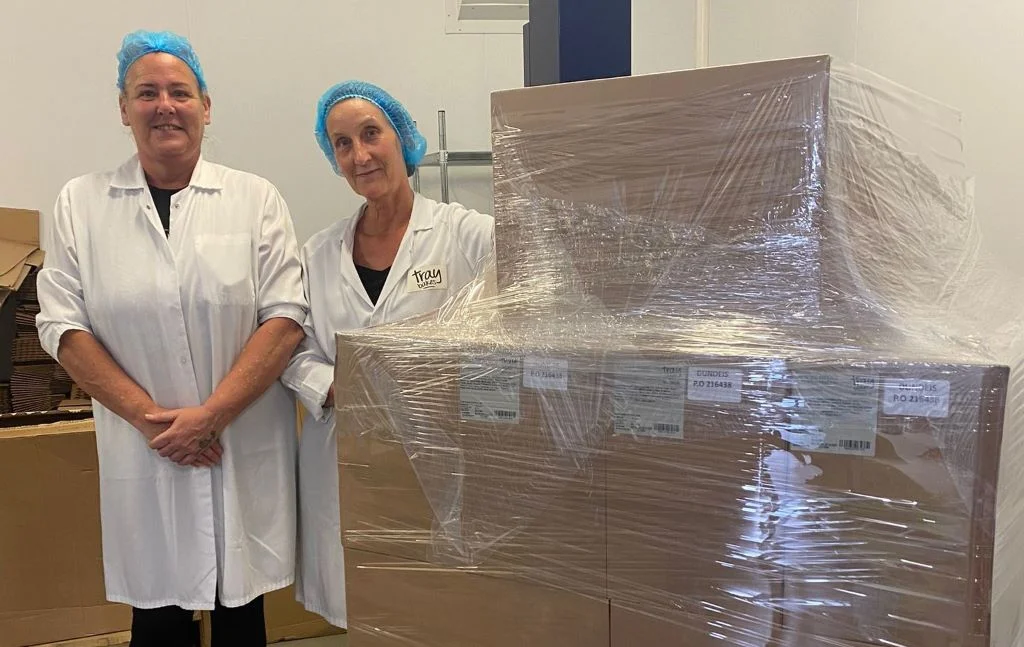 Two women in hairnets with pallet of boxes.