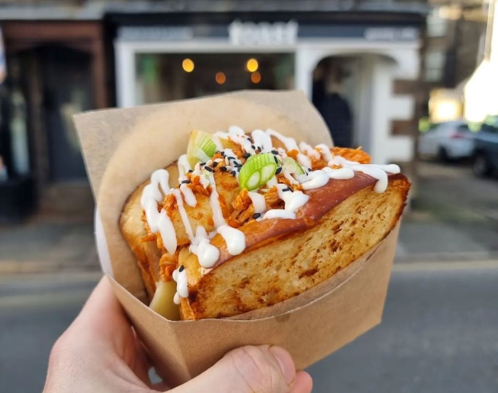 Hand holding sandwich with sauce and onions