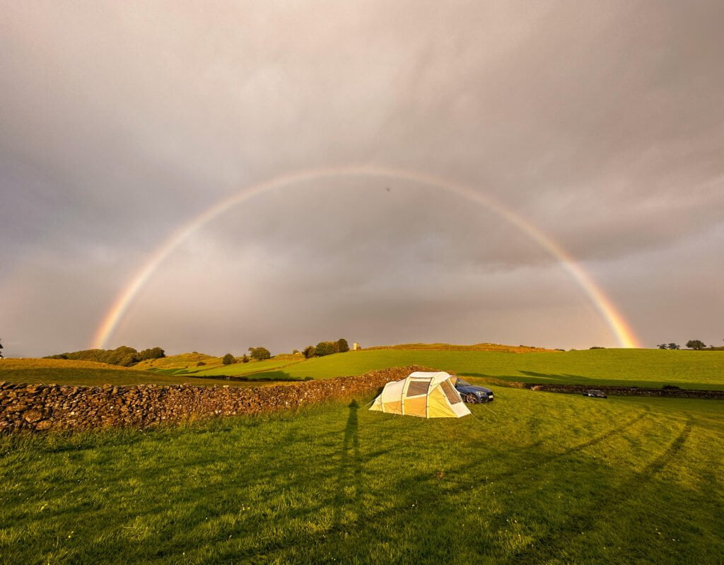 Bright rainbow over countryside with a tent