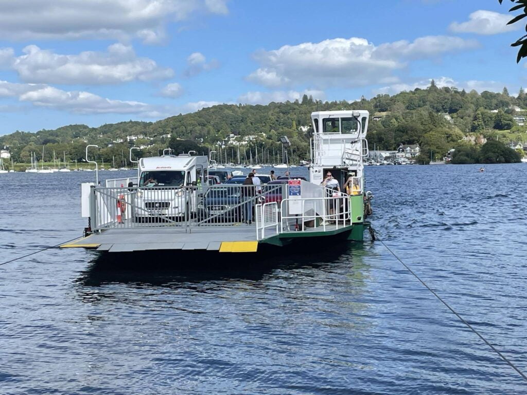 Cars and people on a ferry across a lake.