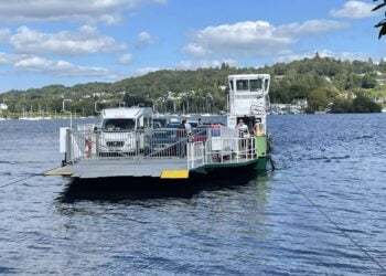 Cars and people on a ferry across a lake.