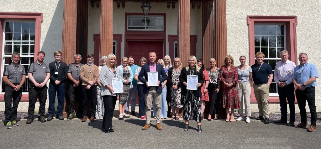 Group photo of people holding certificates outside building.