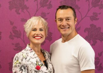 Smiling couple in front of floral wallpaper.