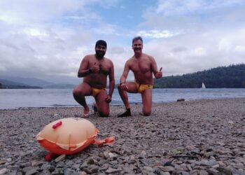 Two men kneeling on rocky beach by the lake.