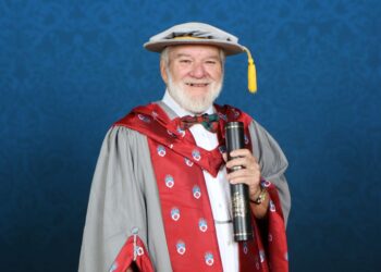 Elderly man in graduation gown holding diploma