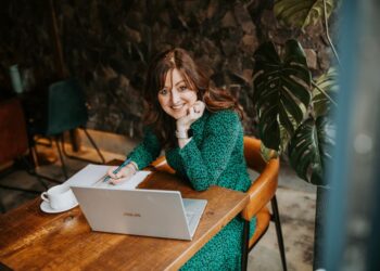 Woman working at a café with laptop and notebook.