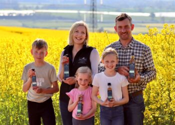 Family holding bottles in rapeseed field.