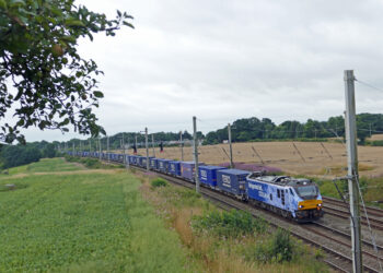 Freight train carrying containers through countryside.