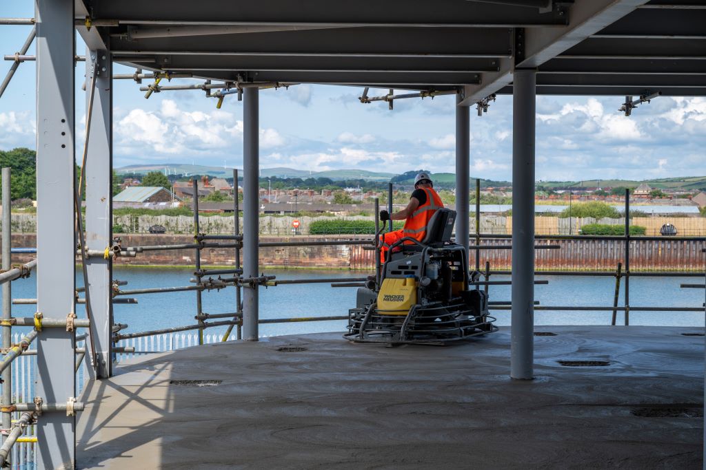 Worker on concrete trowel machine at construction site.