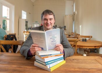 Man reading 'The Power of Now' book in cafe.
