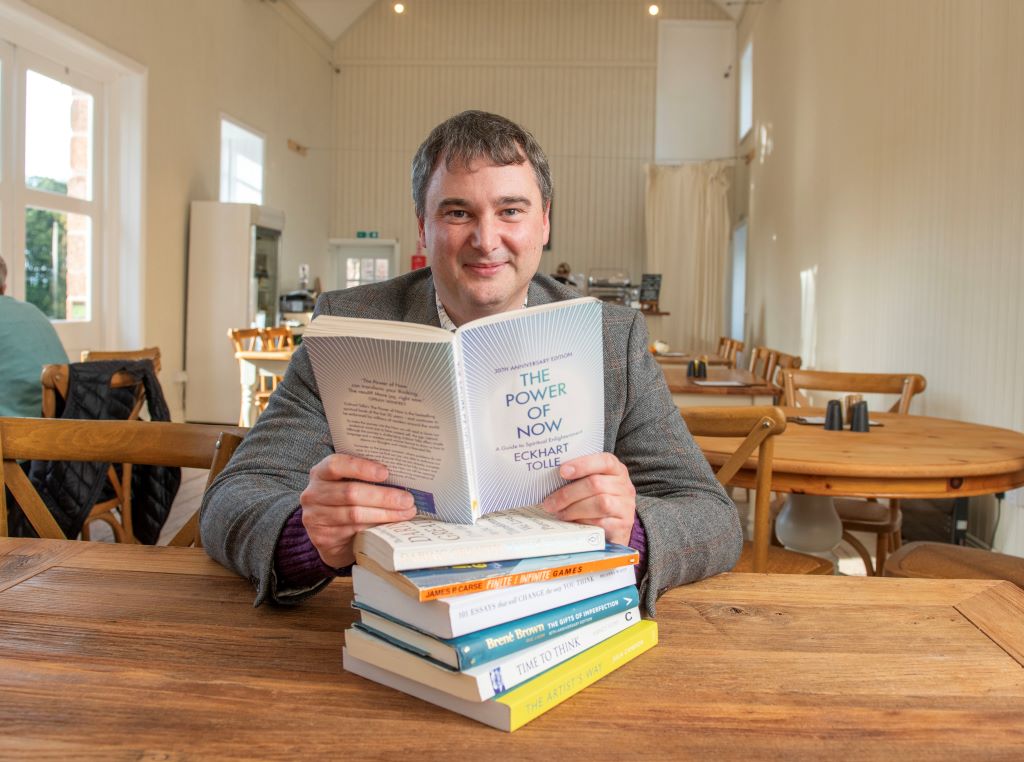 Man reading 'The Power of Now' book in cafe.
