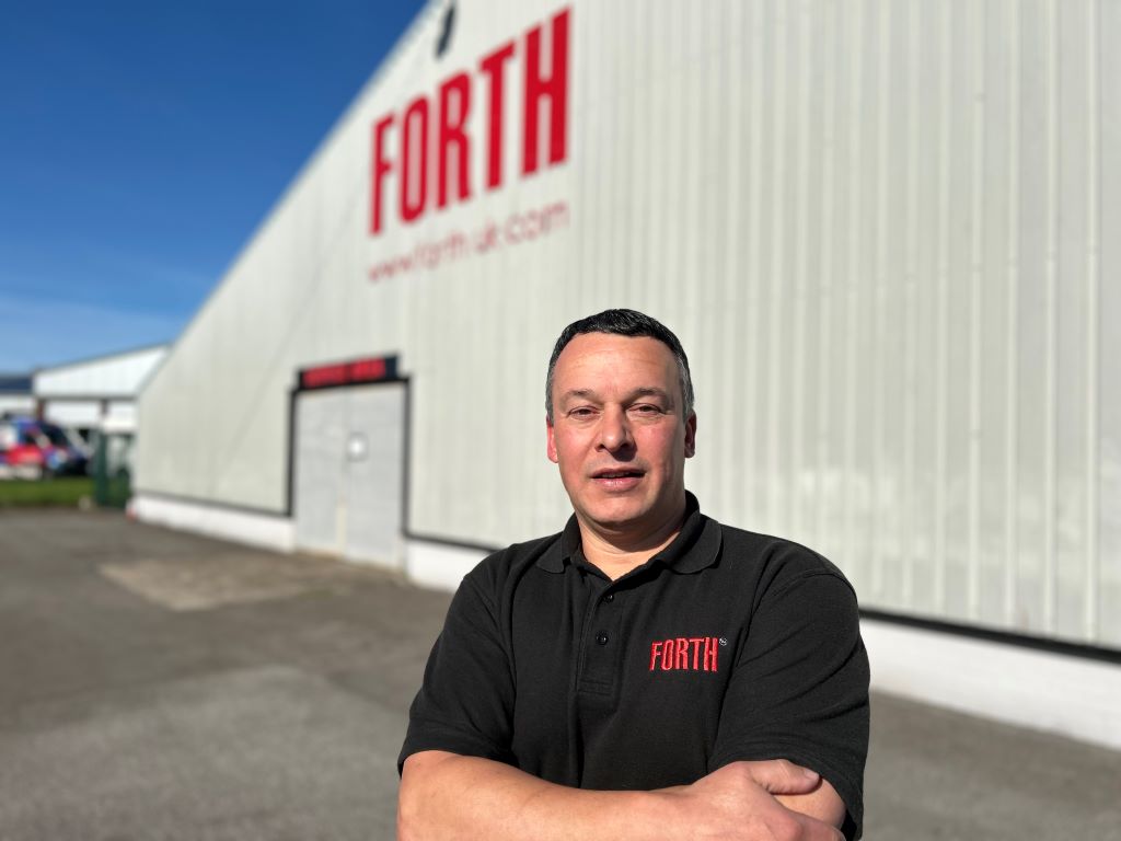 Man stands in front of industrial building, sunny day.