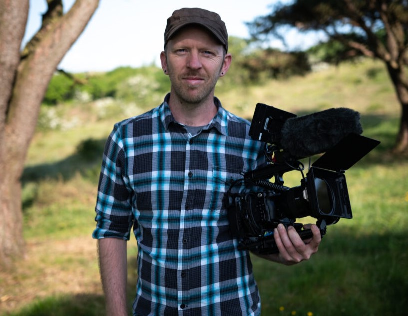 Man holding camera in scenic outdoor setting.