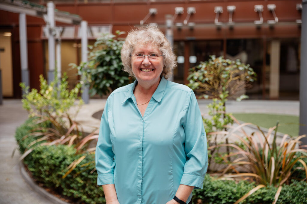 Smiling person in blue shirt, outdoor garden backdrop.