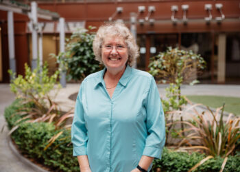 Smiling person in blue shirt, outdoor garden backdrop.