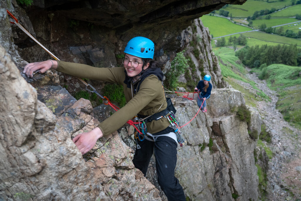 Two climbers scaling a rocky cliff edge with ropes.