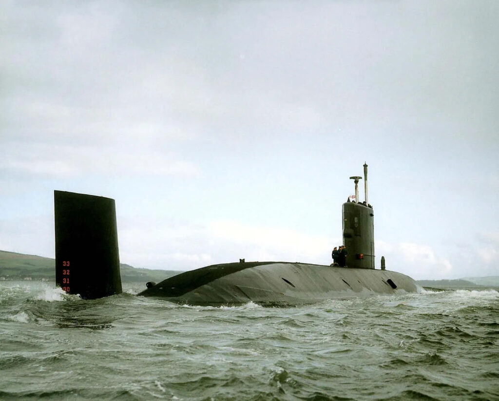 Navy submarine surfaced in open water near coastline.