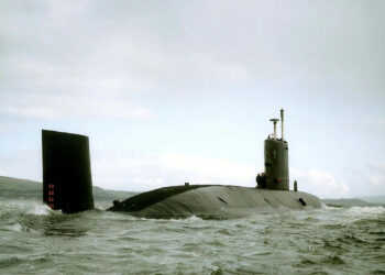 Navy submarine surfaced in open water near coastline.