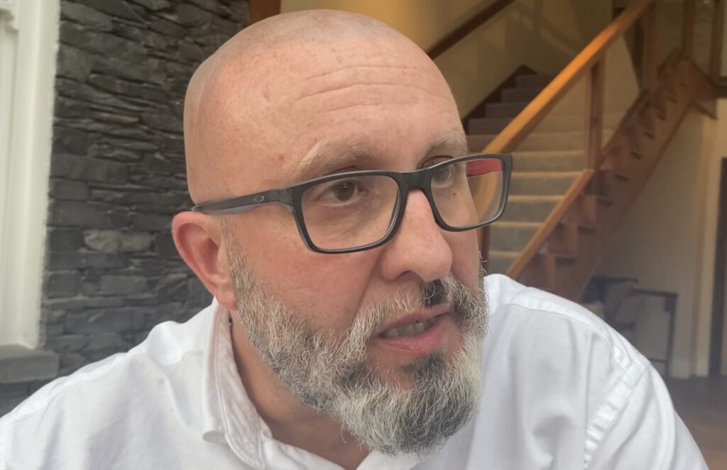 Man with glasses and beard indoors, close-up view.