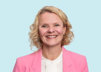 Smiling person in pink blazer on blue background.