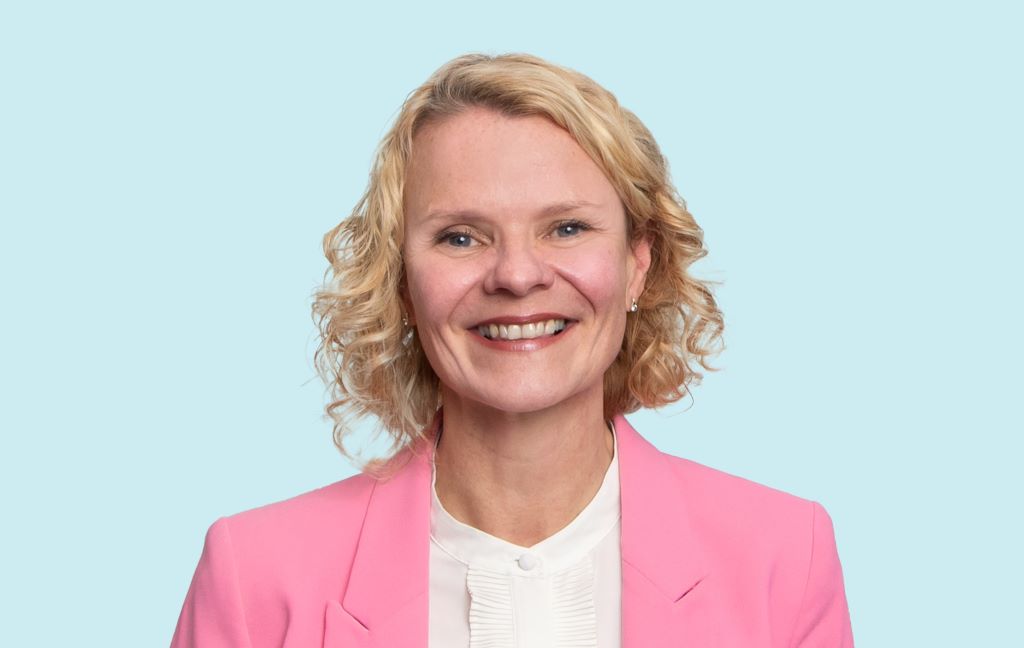 Smiling person in pink blazer on blue background.