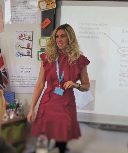 Teacher presenting in a classroom with a slideshow.