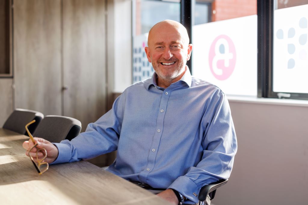 Smiling man holding glasses in office setting.