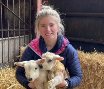 Person holding two lambs in a barn