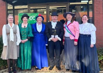 Group in historical costumes outside red brick building.
